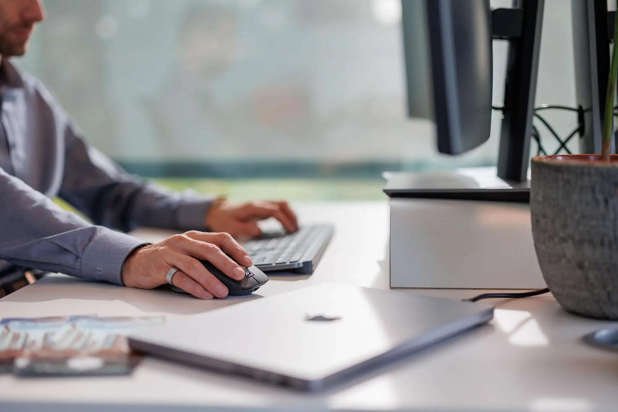 Person arbeitet an einem Schreibtisch mit Tastatur und Maus, Laptop geschlossen im Vordergrund